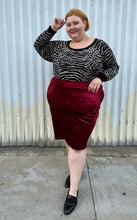 Load image into Gallery viewer, Additional full-body front view of a size 5X SWAK deep red crushed velvet bodycon midi pencil skirt styled with an animal print sweater tucked in and loafers on a size 22/24 model. The photo is taken outside in natural lighting.
