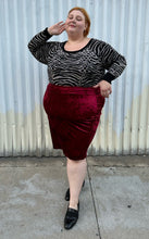 Load image into Gallery viewer, Full-body front view of a size 3 Torrid black and silver metallic thread animal pattern sweater with black piping and cuffs styled tucked into a red crushed velvet bodycon skirt with black loafers on a size 22/24 model. The photo is taken outside in natural lighting.

