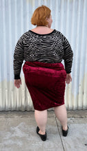 Load image into Gallery viewer, Full-body back view of a size 5X SWAK deep red crushed velvet bodycon midi pencil skirt styled with an animal print sweater tucked in and loafers on a size 22/24 model. The photo is taken outside in natural lighting.
