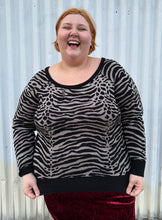 Load image into Gallery viewer, Additional front view of a size 3 Torrid black and silver metallic thread animal pattern sweater with black piping and cuffs styled with a red crushed velvet bodycon skirt on a size 22/24 model. The photo is taken outside in natural lighting.
