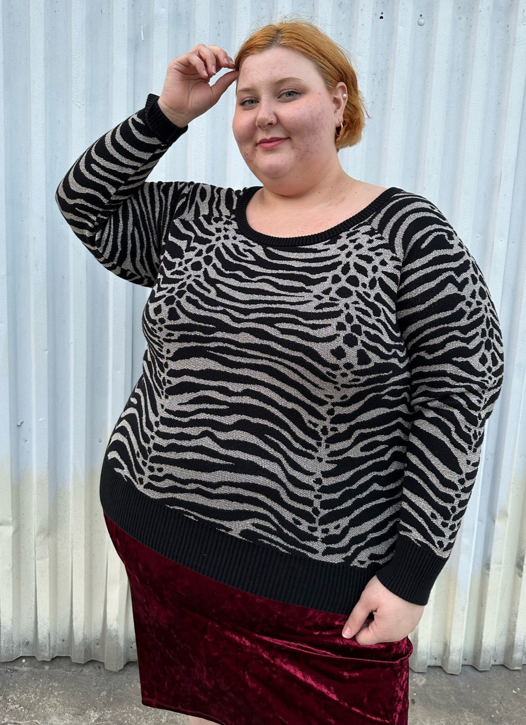Front view of a size 3 Torrid black and silver metallic thread animal pattern sweater with black piping and cuffs styled with a red crushed velvet bodycon skirt on a size 22/24 model. The photo is taken outside in natural lighting.