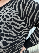Load image into Gallery viewer, Close up view of the black and silver mixed animal pattern of a size 3 Torrid black and silver metallic thread animal pattern sweater with black piping and cuffs on a size 22/24 model. The photo is taken outside in natural lighting.
