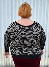 Load image into Gallery viewer, Back view of a size 3 Torrid black and silver metallic thread animal pattern sweater with black piping and cuffs styled with a red crushed velvet bodycon skirt on a size 22/24 model. The photo is taken outside in natural lighting.
