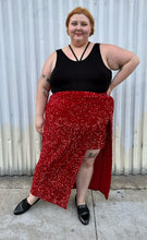 Load image into Gallery viewer, Additional full-body front view of a size 24 Eloquii red sequin twist-detail maxi skirt with high open slit and mini slip skirt underneath styled with a black criss-cross top and black loafers on a size 22/24 model. The photo is taken outside in natural lighting.
