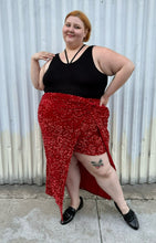 Load image into Gallery viewer, Final full-body front view of a size 24 Eloquii red sequin twist-detail maxi skirt with high open slit and mini slip skirt underneath styled with a black criss-cross top and black loafers on a size 22/24 model. The photo is taken outside in natural lighting.
