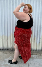 Load image into Gallery viewer, Full-body side view of a size 24 Eloquii red sequin twist-detail maxi skirt with high open slit and mini slip skirt underneath styled with a black criss-cross top and black loafers on a size 22/24 model. The photo is taken outside in natural lighting.
