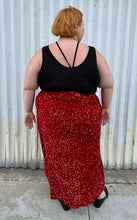 Load image into Gallery viewer, Full-body back view of a size 24 Eloquii red sequin twist-detail maxi skirt with high open slit and mini slip skirt underneath styled with a black criss-cross top and black loafers on a size 22/24 model. The photo is taken outside in natural lighting.
