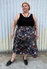 Load image into Gallery viewer, Additional full-body front view of a size 24 Eloquii black pleather maxi skirt with cool-toned floral all-over pattern styled with a black criss-cross tank tucked in and black loafers on a size 22/24 model. The photo is taken outside in natural lighitng.
