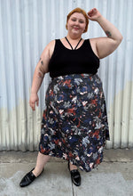 Load image into Gallery viewer, Final full-body front view of a size 24 Eloquii black pleather maxi skirt with cool-toned floral all-over pattern styled with a black criss-cross tank tucked in and black loafers on a size 22/24 model. The photo is taken outside in natural lighitng.
