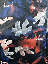 Load image into Gallery viewer, Close up view of the cool-toned (silver, blue, orange) floral leaf pattern of a size 24 Eloquii black pleather maxi skirt with cool-toned floral all-over pattern on a size 22/24 model. The photo is taken outside in natural lighitng.
