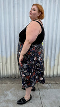 Load image into Gallery viewer, Full-body side view of a size 24 Eloquii black pleather maxi skirt with cool-toned floral all-over pattern styled with a black criss-cross tank tucked in and black loafers on a size 22/24 model. The photo is taken outside in natural lighitng.
