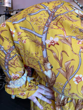 Load image into Gallery viewer, Close up view of the mixed pattern of a size 4X H&amp;M x Johanna Ortiz golden yellow, white, and brown mixed pattern of birds in trees maxi dress with keyhole neckline and back, ruffle hem, and ruffles cuffs. The photo was taken inside under flourescent and natural lighting.
