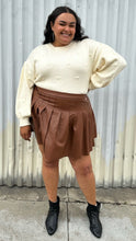 Load image into Gallery viewer, Full-body front view of a size 18/20 Eloquii cream chunky knit sweater with swiss dots styled tucked into a brown pleather mini skirt on a size 18/20 model. The photo is taken outside in natural lighting.
