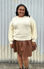 Load image into Gallery viewer, Front view of a size 18/20 Eloquii cream chunky knit sweater with swiss dots styled over a brown pleather mini skirt on a size 18/20 model. The photo is taken outside in natural lighting.
