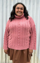Load image into Gallery viewer, Front view of a size 18/20 Eloquii blush pink cable-knit turtleneck sweater with thick fold-over neck and swiss dots styled over a brown pleather mini skirt on a size 18/20 model. The photo is taken outside in natural lighting.
