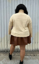 Load image into Gallery viewer, Full-body back view of a size 18/20 Eloquii cream cable-knit turtleneck sweater with thick fold-over neck and swiss dots styled over a brown pleather mini skirt and black boots on a size 18/20 model. The photo is taken outside in natural lighting.
