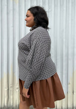 Load image into Gallery viewer, Side view of a size 20 Eloquii black and white patterned sweater with choker neckline and puff sleeves styled over a brown pleather mini skirt on a size 18/20 model. The photo is taken outside in natural lighting.
