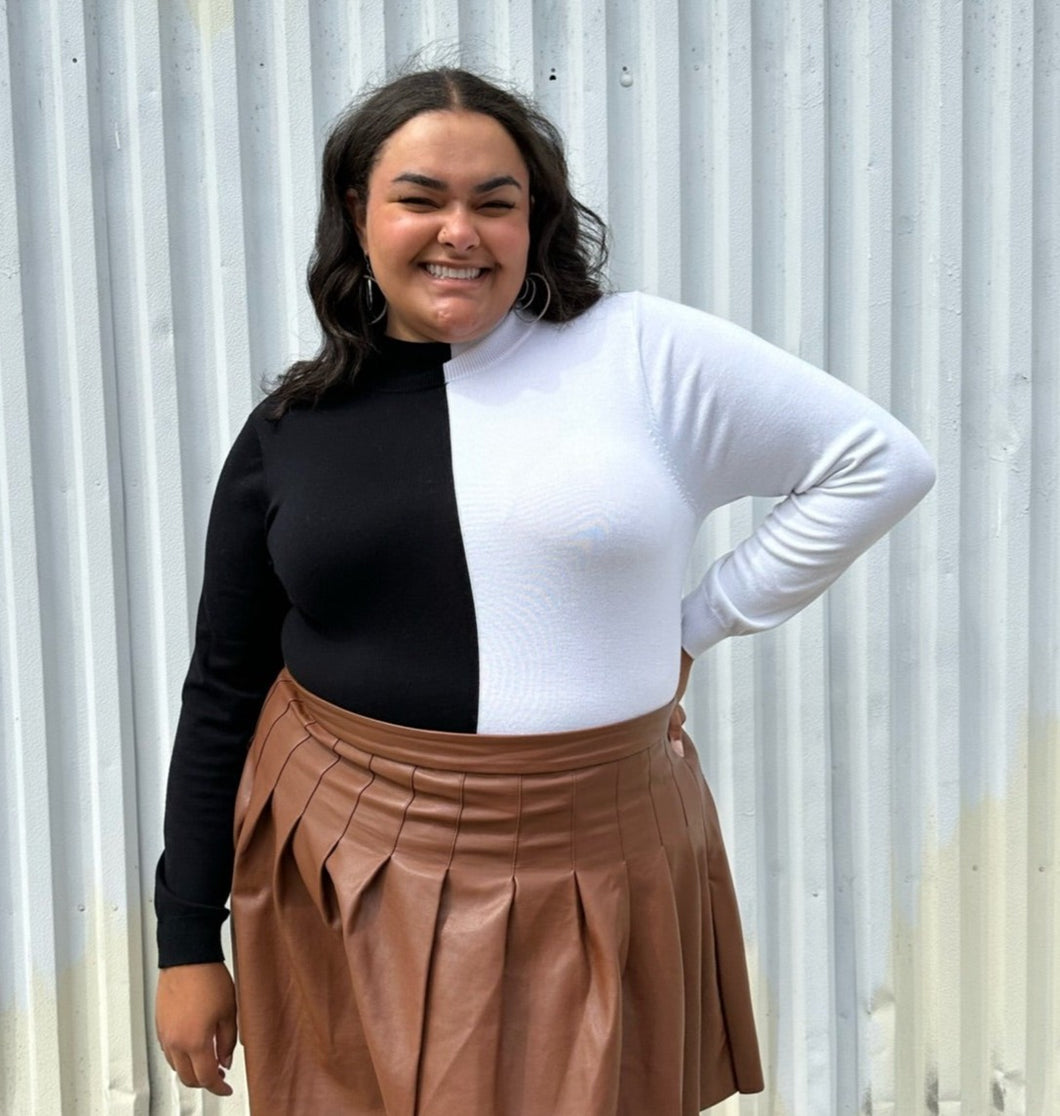 Front view of a size 18/20 Eloquii black and white halfsies long sleeve tee styled tucked into a brown pleather mini skirt on a size 18/20 model. The photo is taken outside in natural lighting.