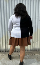 Load image into Gallery viewer, Full-body back view of a size 18/20 Eloquii black and white halfsies long sleeve tee styled over a brown pleather mini skirt with black boots on a size 18/20 model. The photo is taken outside in natural lighting.
