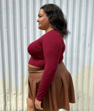 Load image into Gallery viewer, Side view of a size 18/20 maroon long sleeve cropped t-shirt styled over a brown pleather mini skirt on a size 18/20 model. The photo is taken outside in natural lighting.

