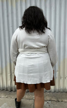 Load image into Gallery viewer, Back view of a size 18/20 Eloquii off-white longline sweater with side slits, a tie belt, subtle puff sleeves, and a v neck styled over a brown pleather mini skirt on a size 18/20 model. The photo is taken outside in natural lighting.
