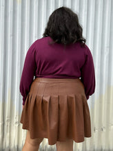 Load image into Gallery viewer, Back view of a size 18/20 Eloquii berry pink longline sweater with side slits, a tie belt, subtle puff sleeves, and a v neck styled tucked into a brown pleather mini skirt on a size 18/20 model. The photo is taken outside in natural lighting.
