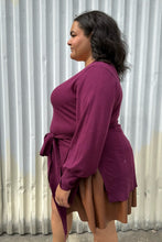 Load image into Gallery viewer, Side view of a size 18/20 Eloquii berry pink longline sweater with side slits, a tie belt, subtle puff sleeves, and a v neck styled over a brown pleather mini skirt on a size 18/20 model. The photo is taken outside in natural lighting.
