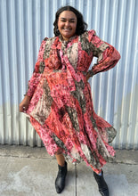 Load image into Gallery viewer, Full-body front view of a 18 Rachel Parcell pink, coral, brown, and cream patchwork floral pattern with pleated skirt, pussy bow, and bishop sleeve styled with the pussy bow tied and black boots on a size 18/20 model. The photo is taken outside in natural lighting.
