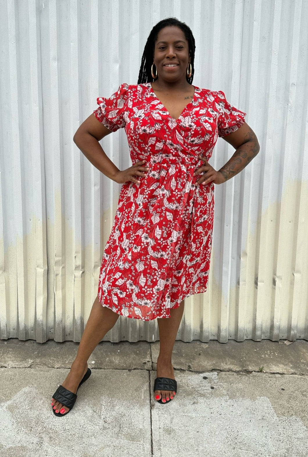 Full-body front view of a size L Chelsea28 red, white, and black floral wrap midi dress with subtle ruffles and puff at the shoulders styled with black slides on a size 14/16 model. The photo is taken outside in natural lighting.