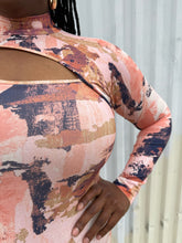 Load image into Gallery viewer, Close up on the abstract pattern and asymmetrical cut-out detail at the bust of a size 0X Nina Parker peach, orange, cream, and purple abstract pattern asymmetrical cut-out bust long sleeve bodycon midi dress on a size 14/16 model. The photo is taken outside in natural lighting.
