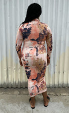 Load image into Gallery viewer, Full-body back view of a size 0X Nina Parker peach, orange, cream, and purple abstract pattern asymmetrical cut-out bust long sleeve bodycon midi dress styled with black slides on a size 14/16 model. The photo is taken outside in natural lighting.
