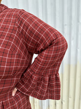 Load image into Gallery viewer, Close up view of  the bell sleeve of a size 3 Torrid brick red plaid pattern bell sleeve button-up shirt dress on a size 22/24 model. The photo is taken outside in natural lighting.
