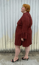 Load image into Gallery viewer, Full-body side view of size 3 Torrid brick red plaid pattern bell sleeve button-up shirt dress styled with black heels on a size 22/24 model. The photo is taken outside in natural lighting.
