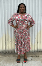 Load image into Gallery viewer, Additional full-body front view of a size L RAGA red, green, and white rose patterned pleated maxi dress styled with black slides on a size 14/16 model. The photo is taken outside in natural lighting.
