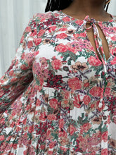 Load image into Gallery viewer, Close up on the rose pattern of a size L RAGA red, green, and white rose patterned pleated maxi dress on a size 14/16 model. The photo is taken outside in natural lighting.
