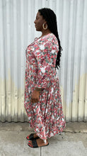 Load image into Gallery viewer, Full-body side view of a size L RAGA red, green, and white rose patterned pleated maxi dress styled with black slides on a size 14/16 model. The photo is taken outside in natural lighting.
