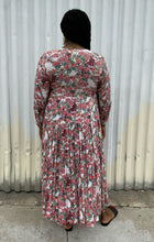 Load image into Gallery viewer, Full-body back view of a size L RAGA red, green, and white rose patterned pleated maxi dress styled with black slides on a size 14/16 model. The photo is taken outside in natural lighting.
