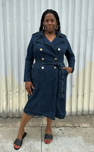 Load image into Gallery viewer, Additional full-body front view of a size 14/16 Eloquii dark wash denim trench coat dress with light brown buttons and tie belt styled with black slides on a size 14/16 model. The photo is taken outside in natural lighting.
