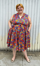 Load image into Gallery viewer, Full-body front view of a size 3X Miss Lulo blue, yellow, and red mixed floral print collared midi dress with fabric buttons and a matching belt styled with gold flats on a size 22/24 model. The photo is taken outside in natural lighting.
