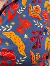 Load image into Gallery viewer, Close up view of the mixed floral pattern of a size 3X Miss Lulo blue, yellow, and red mixed floral print collared midi dress with fabric buttons and a matching belt on a size 22/24 model. The photo is taken outside in natural lighting.

