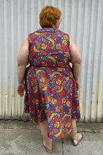 Load image into Gallery viewer, Full-body back view of a size 3X Miss Lulo blue, yellow, and red mixed floral print collared midi dress with fabric buttons and a matching belt styled with gold flats on a size 22/24 model. The photo is taken outside in natural lighting.
