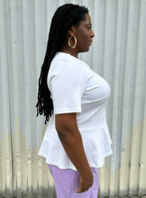 Load image into Gallery viewer, Side view of a size 16 Eloquii white tee with ruffle hem and asymmetrical stitching detail styled with lavender pleather pants on a size 14/16 model. The photo is taken outside in natural lighting.
