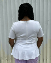 Load image into Gallery viewer, Back view of a size 16 Eloquii white tee with ruffle hem and asymmetrical stitching detail styled with lavender pleather pants on a size 14/16 model. The photo is taken outside in natural lighting.
