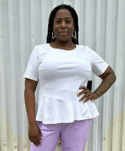 Load image into Gallery viewer, Additional front view of a size 16 Eloquii white tee with ruffle hem and asymmetrical stitching detail styled with lavender pleather pants on a size 14/16 model. The photo is taken outside in natural lighting.
