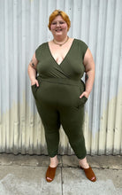 Load image into Gallery viewer, Additional full-body front view of a size 3X Lillian olive green v-neck stretchy jumpsuit with pockets styled with brown mules on a size 22/24 model. The photo is taken outside in natural lighting.
