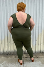 Load image into Gallery viewer, Full-body back view of a size 3X Lillian olive green v-neck stretchy jumpsuit with pockets styled with brown mules on a size 22/24 model. The photo is taken outside in natural lighting.
