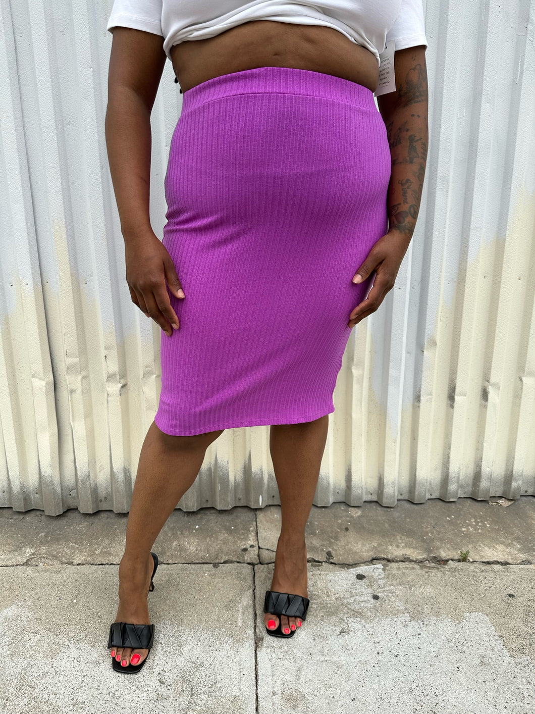 Front view of a size 14/16 Eloquii light purple ribbed pencil skirt styled with black heels and a white top on a size 14/16 model. The photo was taken outside in natural lighting.