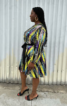 Load image into Gallery viewer, Full-body side view of a size 16 Eloquii yellow, blue, purple, pink and green sequin striped wrap dress with black belt styled with black heels on a size 14/16 model. The photo is taken outside in natural lighting.

