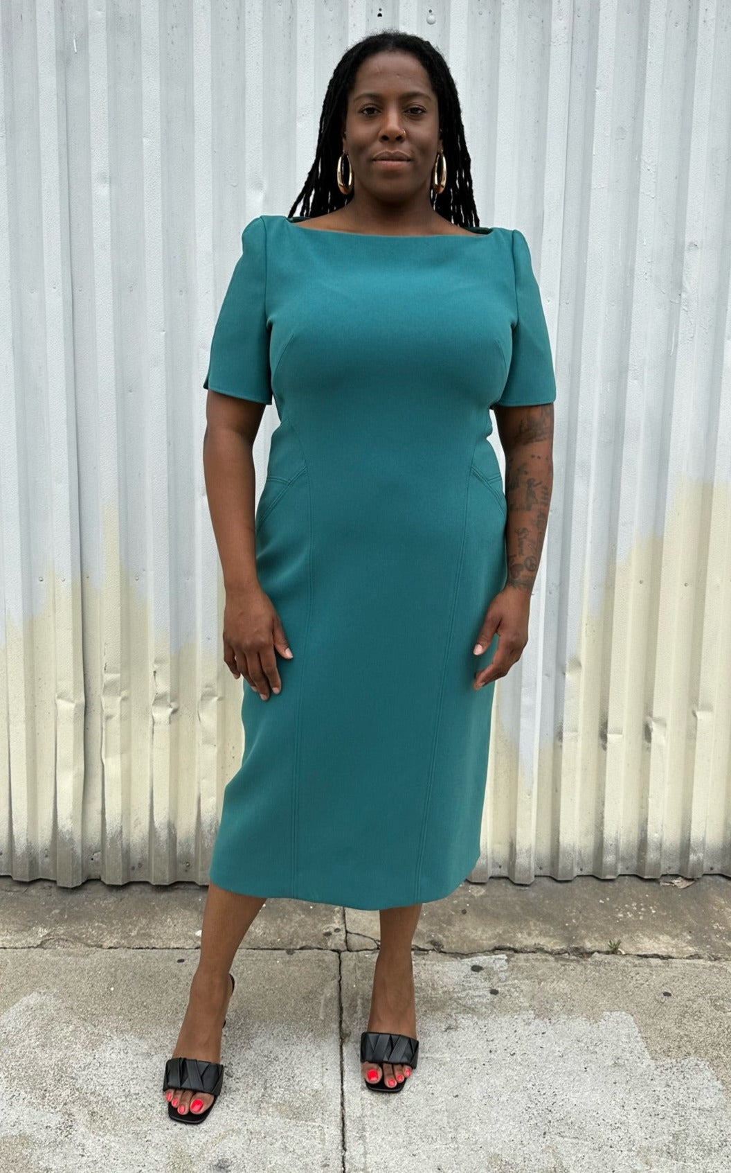 Full-body front view of a size 16 Zac Posen via 11 Honoré teal boatneck sheath dress styled with black kitten heels on a size 14/16 model. The photo is taken outside in natural lighting.