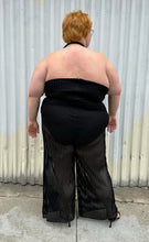 Load image into Gallery viewer, Full-body back view of a size 3 Fashion to Figure black halter sheer mesh vertical striped jumpsuit with a bodysuit lining styled with black heels on a size 22/24 model. The photo is taken outside in natural lighting.
